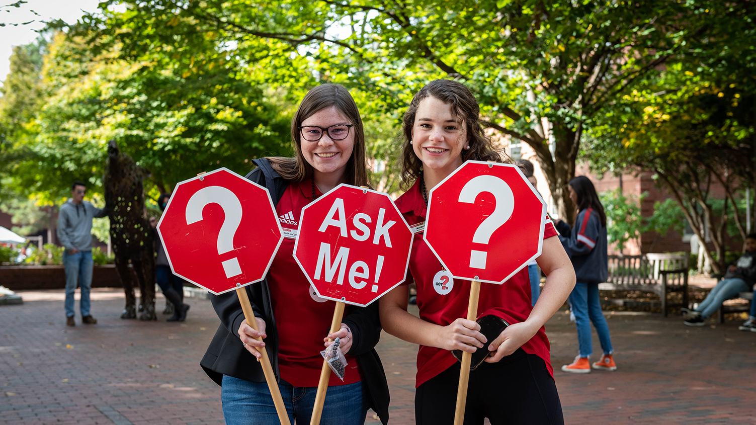 Students holding Ask Me sign in front of copper wolves on NC State Campus