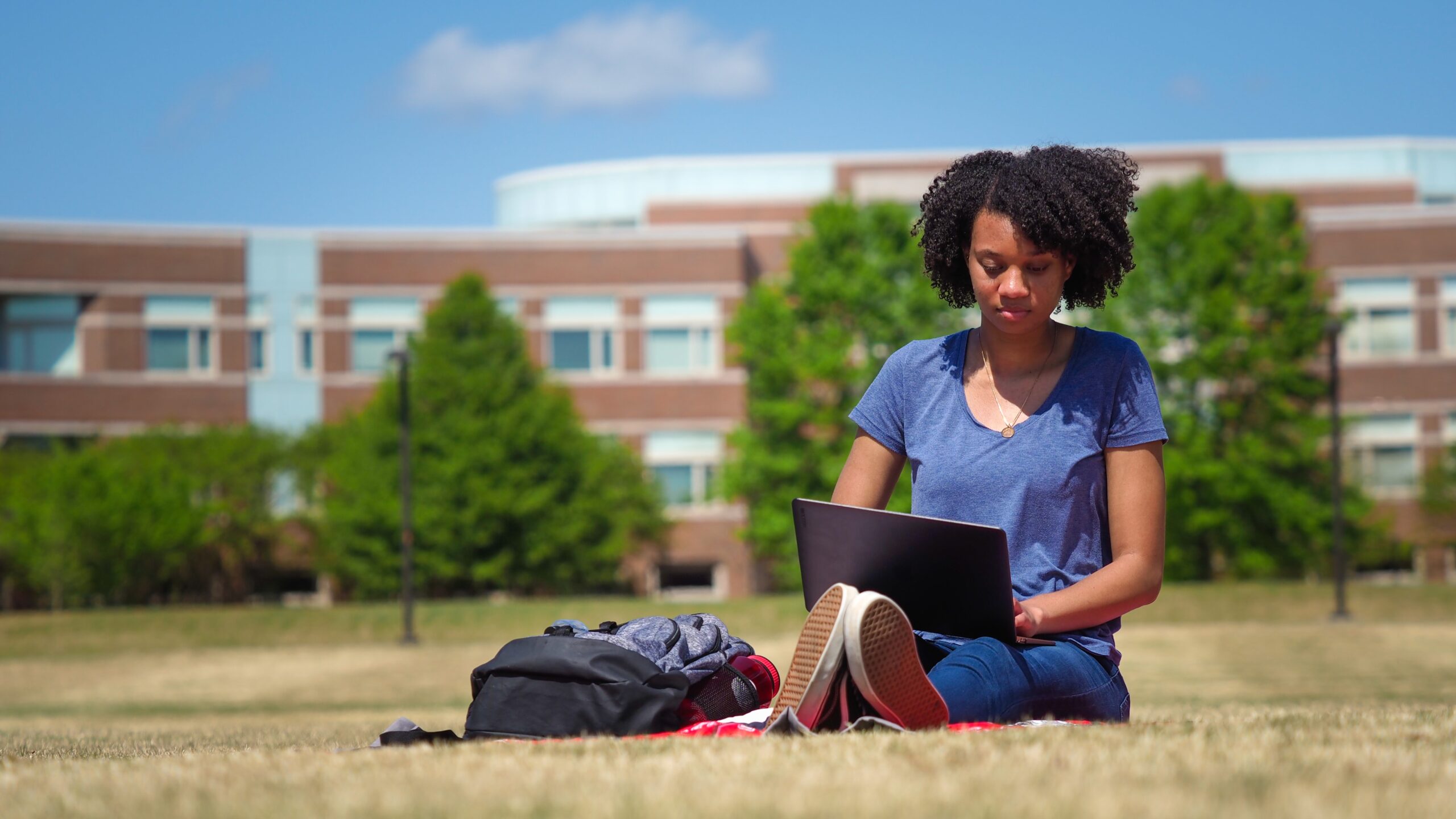 A student sits in a courtyard on Centennial Campus working on a laptop.